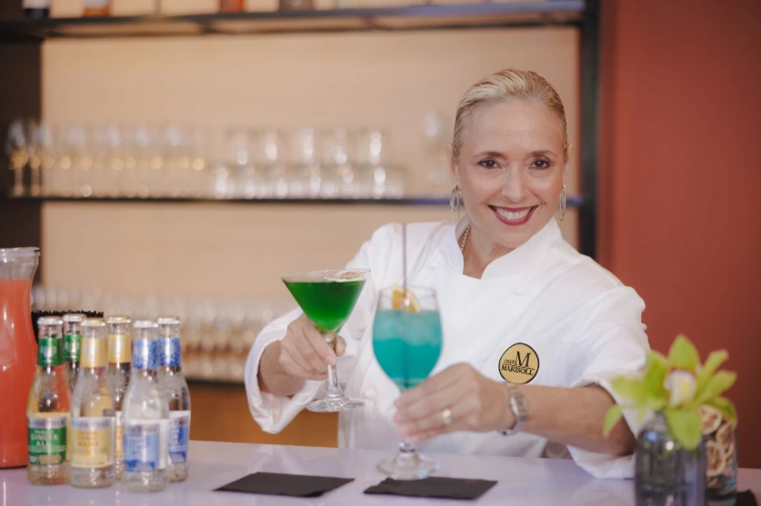 Smiling Chef Marisoll presenting colorful cocktails at a beverage bar during a corporate event.