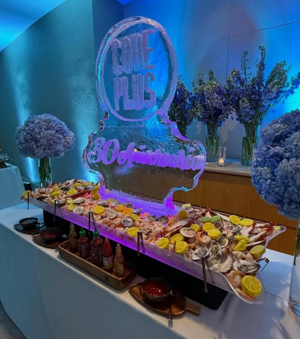 Premium catering table with seafood bar on ice, oysters, shrimp, and elegant floral décor at a nighttime event.